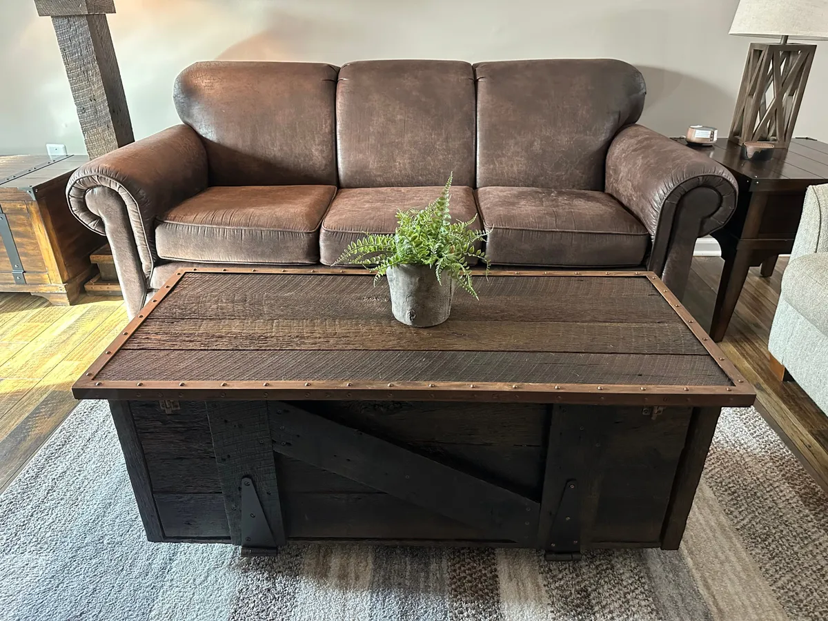 A welcoming living area featuring a brown leather sofa, rustic coffee table, and a potted plant. The room invites conversation and relaxation and is styled with warm, inviting touches that suggest a space for friends to gather after a day out.
