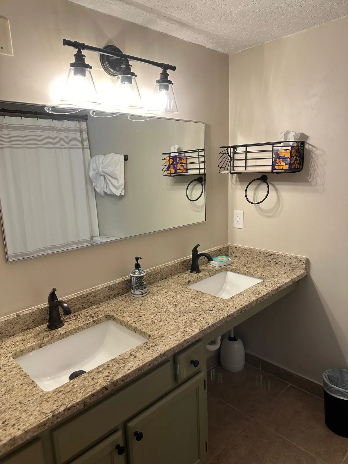 A bright, spacious bathroom with a double sink vanity, large mirror, stylish light fixture, towel rack, and a storage basket. The space feels practical yet inviting, ideal for morning routines or winding down after a day of adventure.