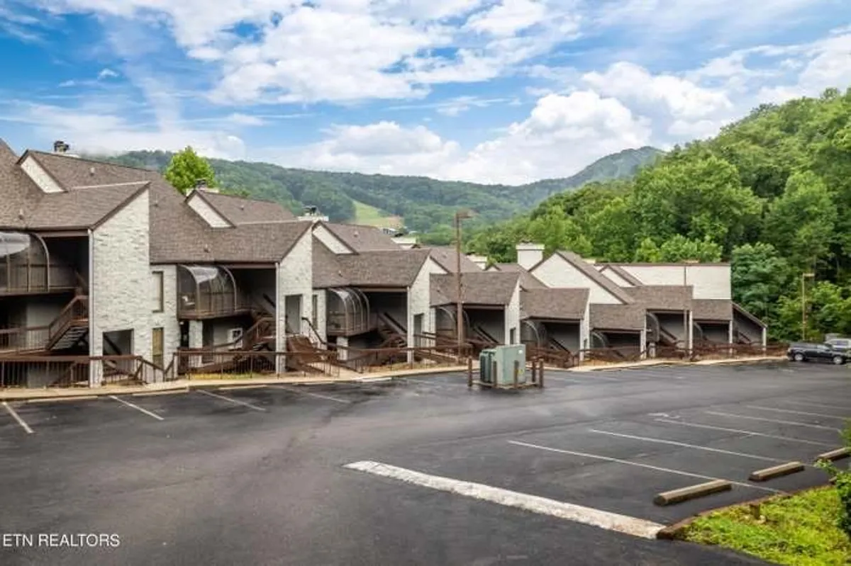 A wide exterior view of multi-unit buildings set against the backdrop of the Smoky Mountains, with open space for outdoor leisure and family gatherings. The setting hints at the community amenities, scenic vistas, and proximity to nature.