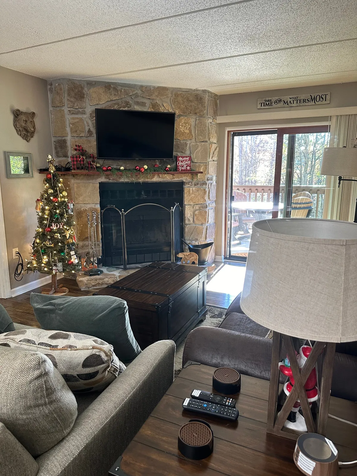 A cozy interior featuring a prominent wood-burning fireplace, a decorated Christmas tree, a coffee table, and a large window. The ambiance is both festive and serene, spotlighting the fireplace as a seasonal centerpiece for comfort and gatherings.